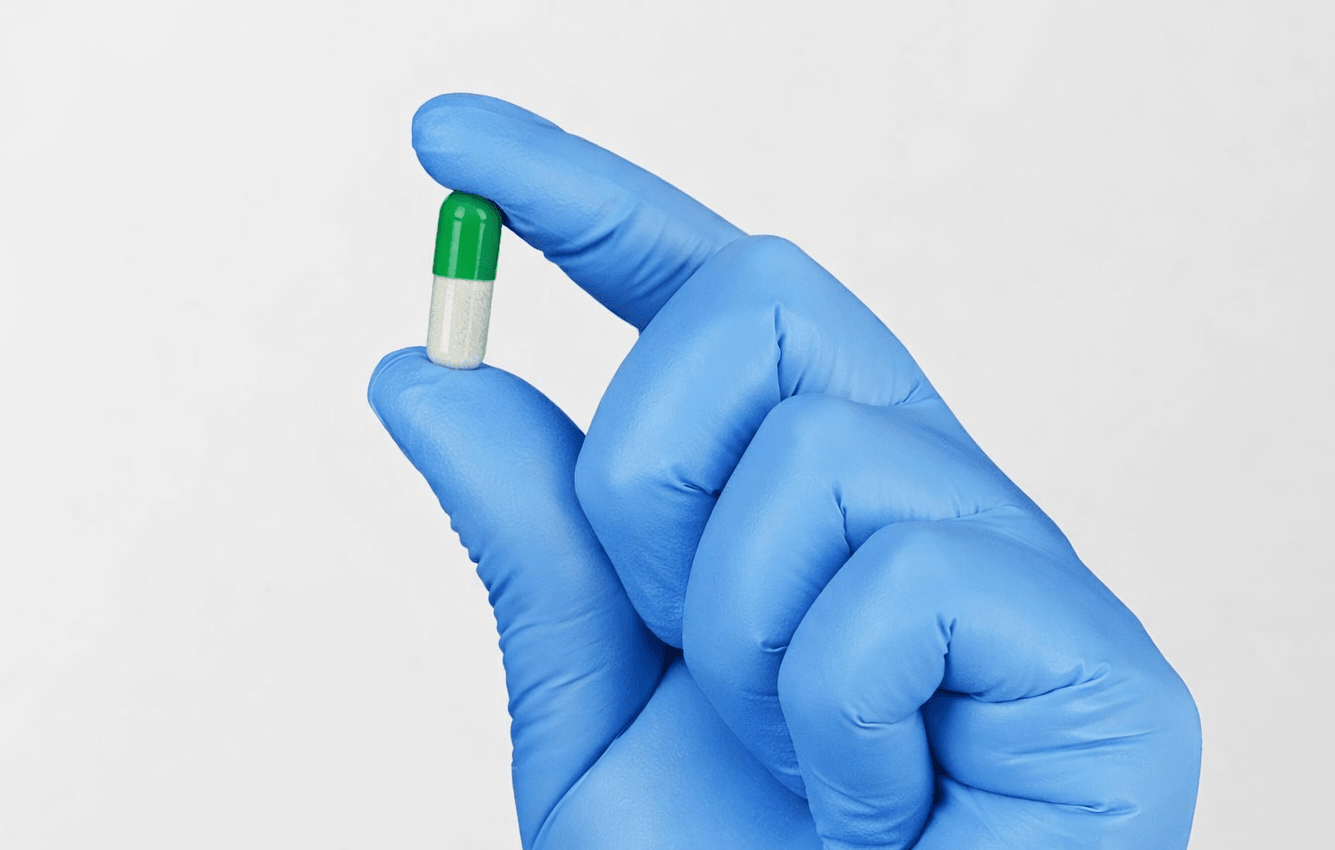 Gloved hand holding medicine capsule